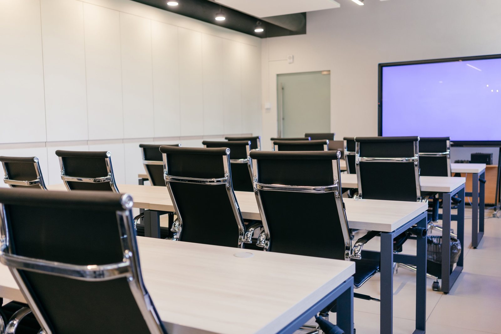 Training room with rows of desks, chairs and a wall-mounted display