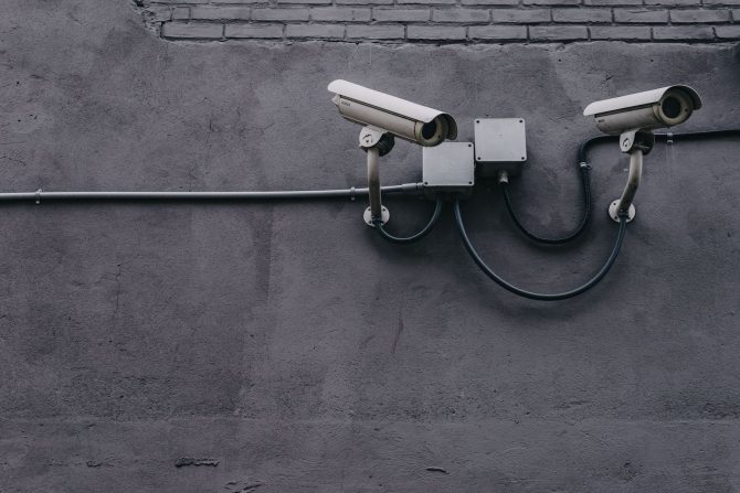 Two bullet surveillance cameras on a concrete wall with conduit-routed cabling