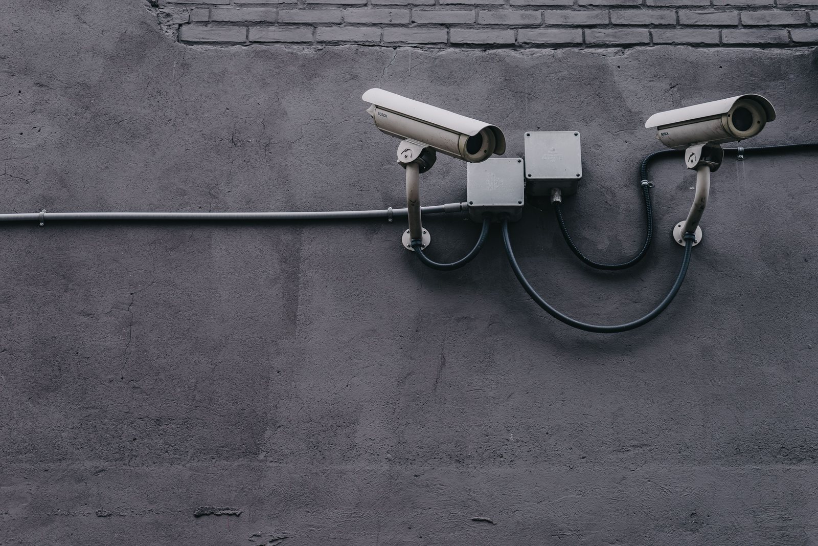 Two bullet surveillance cameras on a concrete wall with conduit-routed cabling