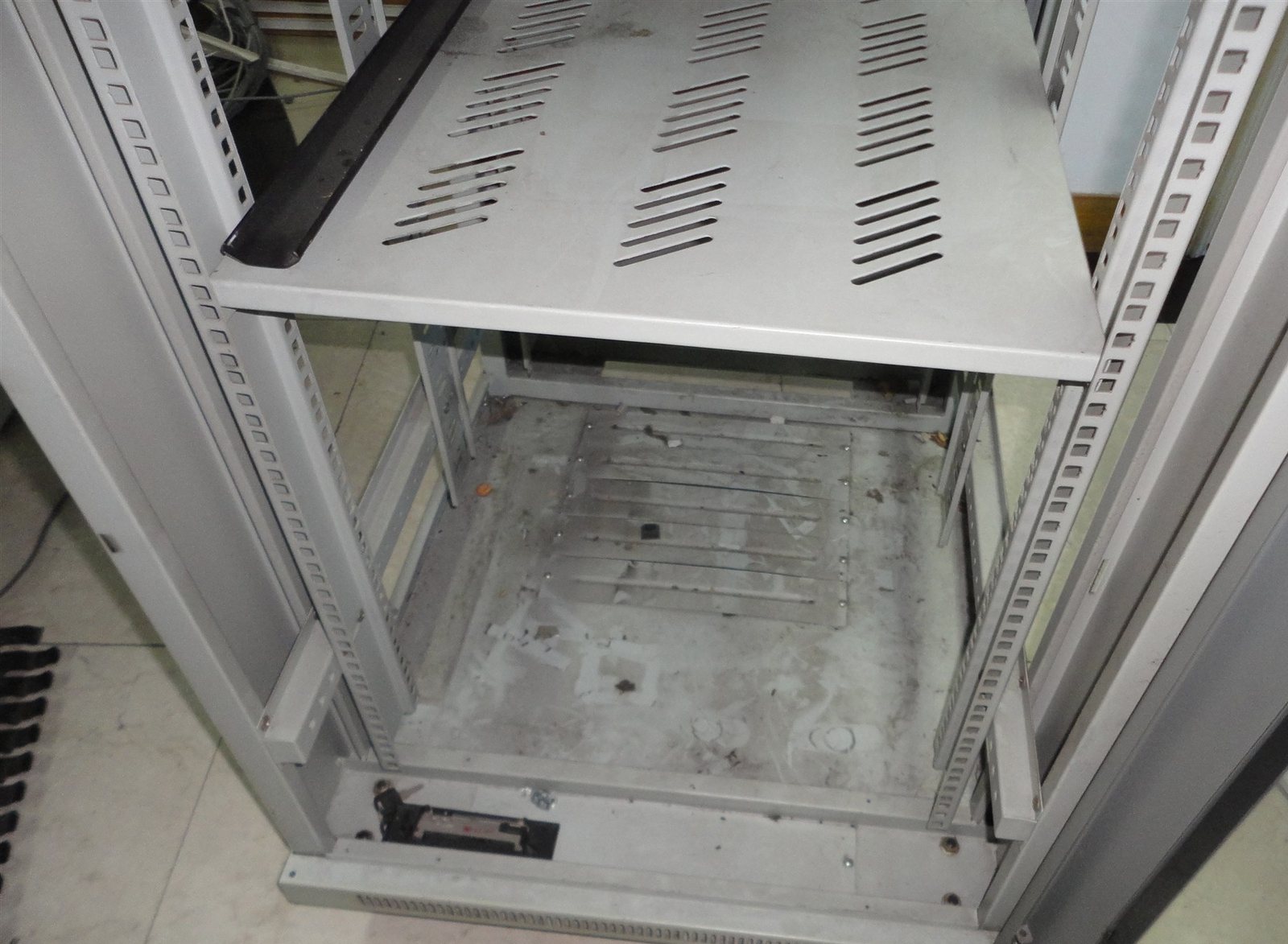Emptied network cabinet after equipment removal, showing shelf, mounting rails and floor cable entry
