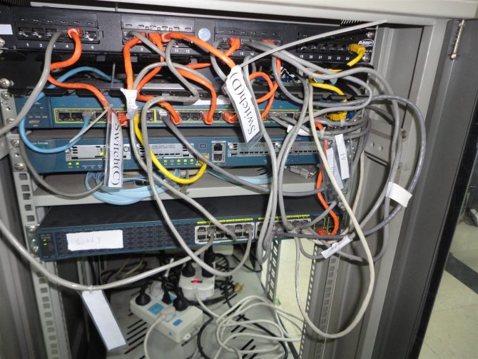 Network cabinet before migration: patch panels, stacked switches and tagged patch cords awaiting re-termination