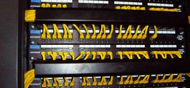 Front of a network rack with labeled copper patch panels, yellow patch leads and horizontal cable managers